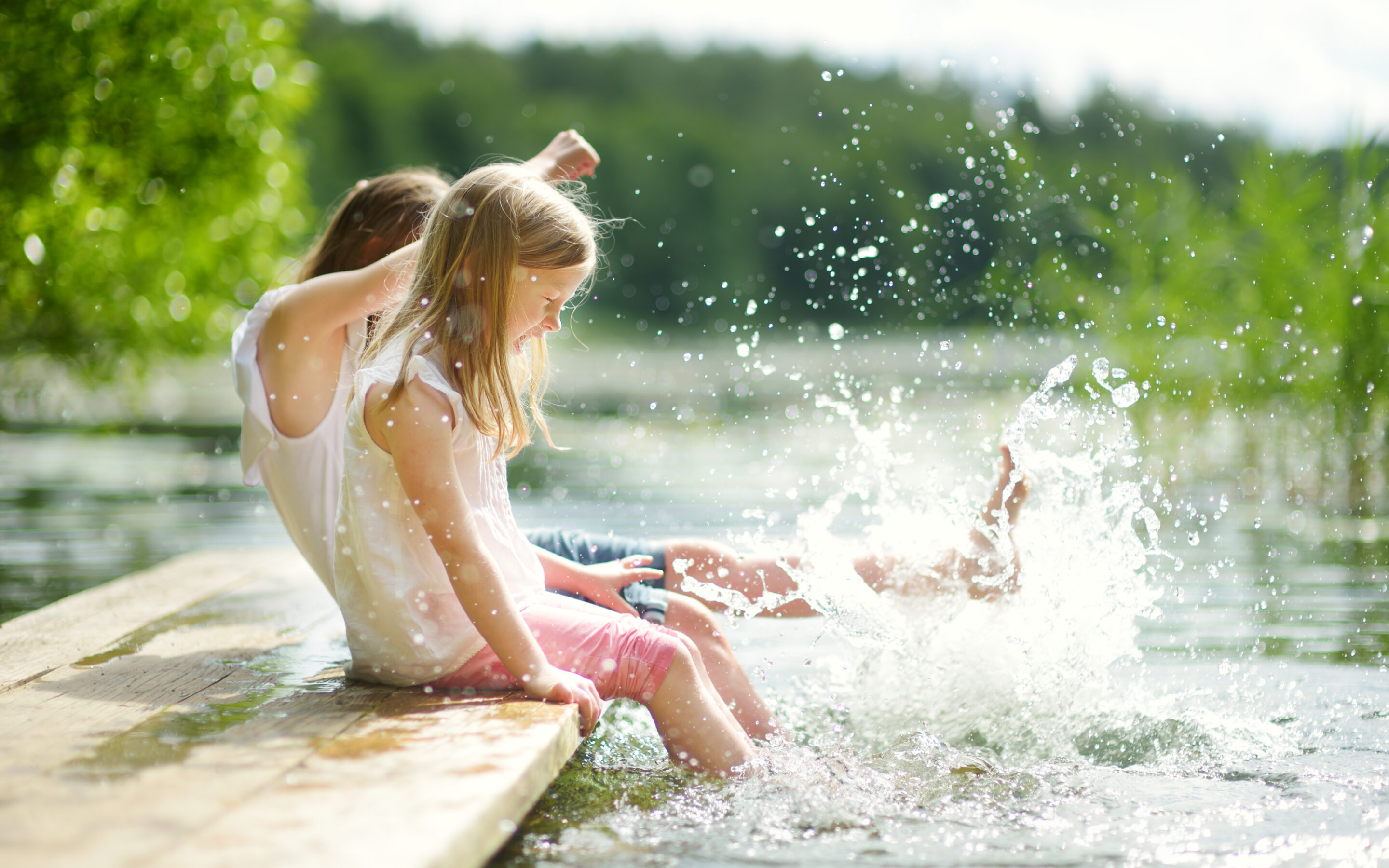 two girls splashing their feet in the lake celebrating summer