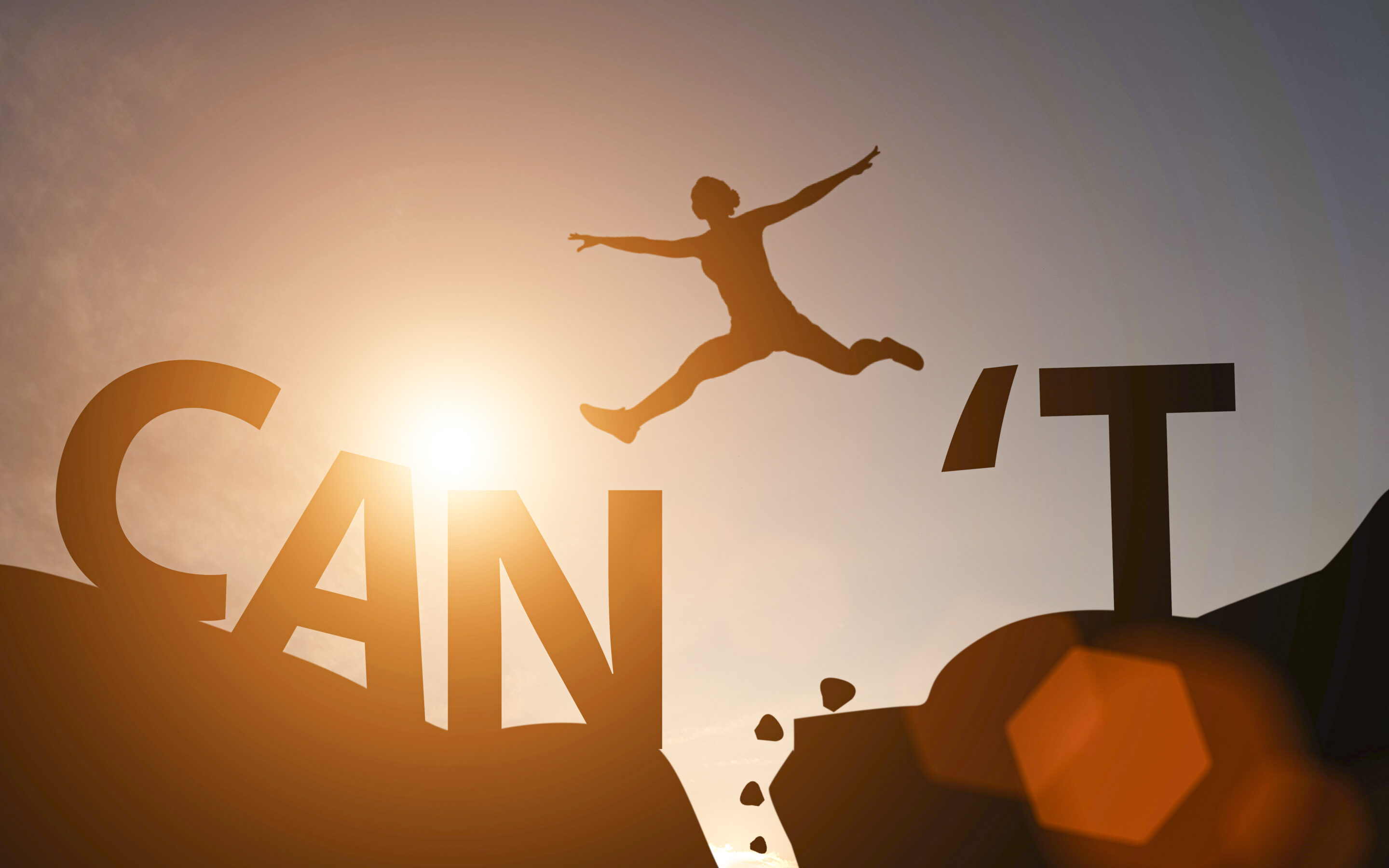 Silhouette of a woman jumping from the word can't to can on a mountain